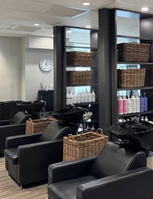Hair salon wash station with black leather chairs, black basins, and wicker baskets.